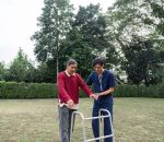 A caring young caregiver assists an elderly man using a walker in a bright garden, promoting mobility and fostering trust in the caregiving relationship.